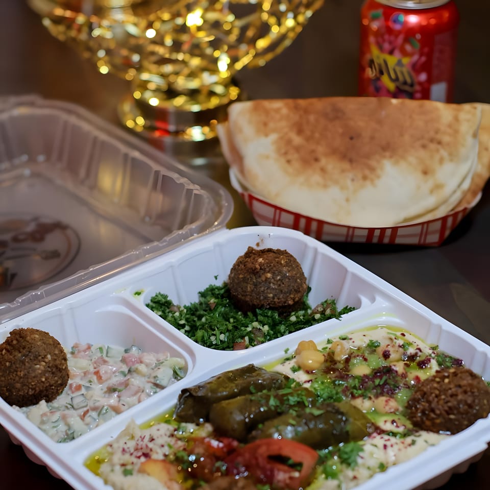 Middle Eastern mezze platter with falafel, hummus, stuffed vegetables, salads, and flatbread beside a colorful soda can.