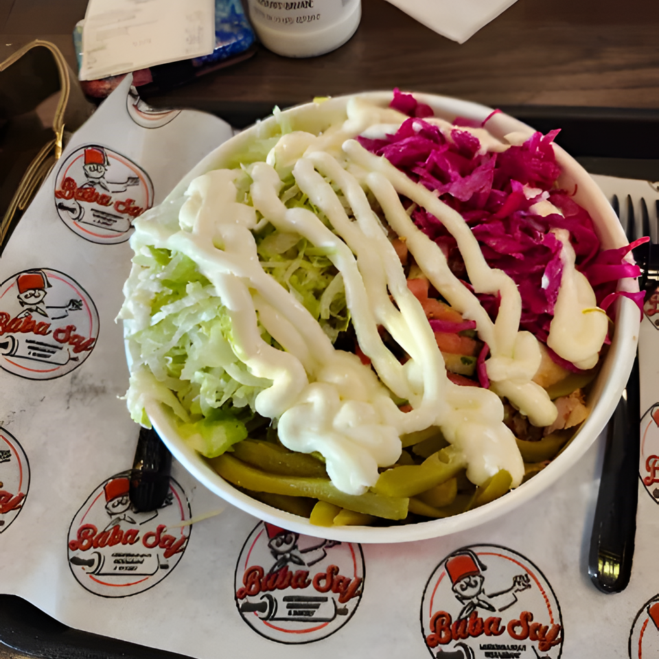 Loaded bowl of lettuce, pickles, shredded purple cabbage, vegetables, and creamy white sauce on Baba’s branded paper.