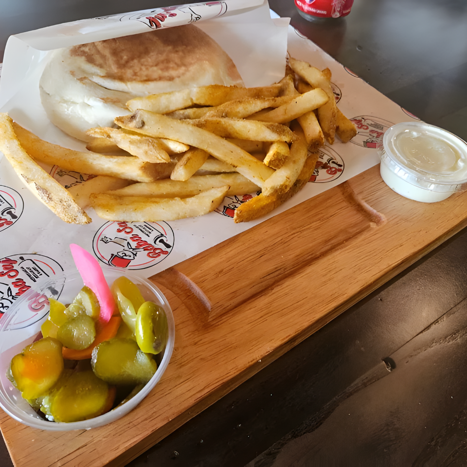 Gyro sandwich with golden fries, pickles, and dipping sauce served on a wooden board.