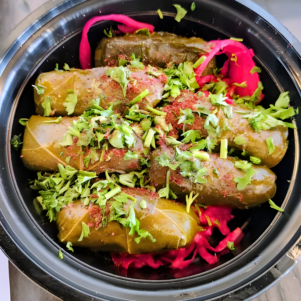 Stuffed grape leaves garnished with fresh herbs and bright pink pickled onions in a black serving dish.