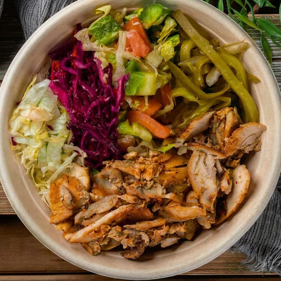 Top-down view of a bowl filled with chicken shawarma, red cabbage, lettuce, and pickled vegetables.