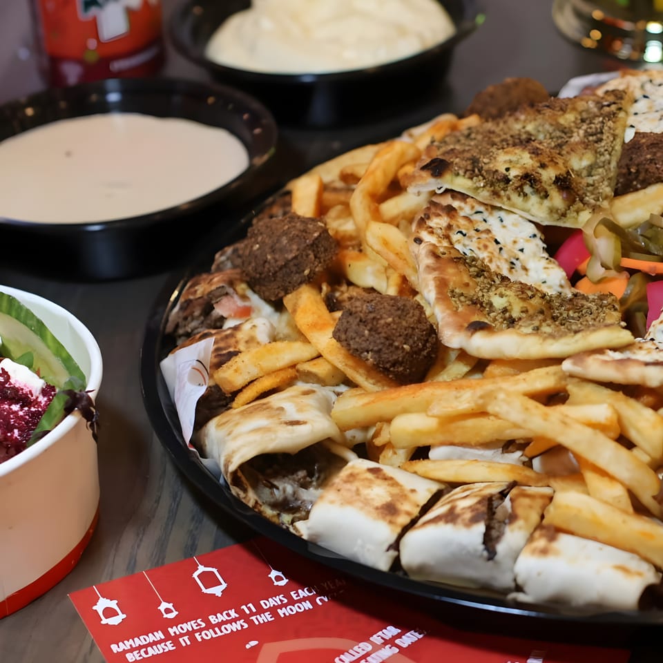 Mediterranean platter with gyros, falafel, pita, fries, salad, and dipping sauces on a restaurant table.